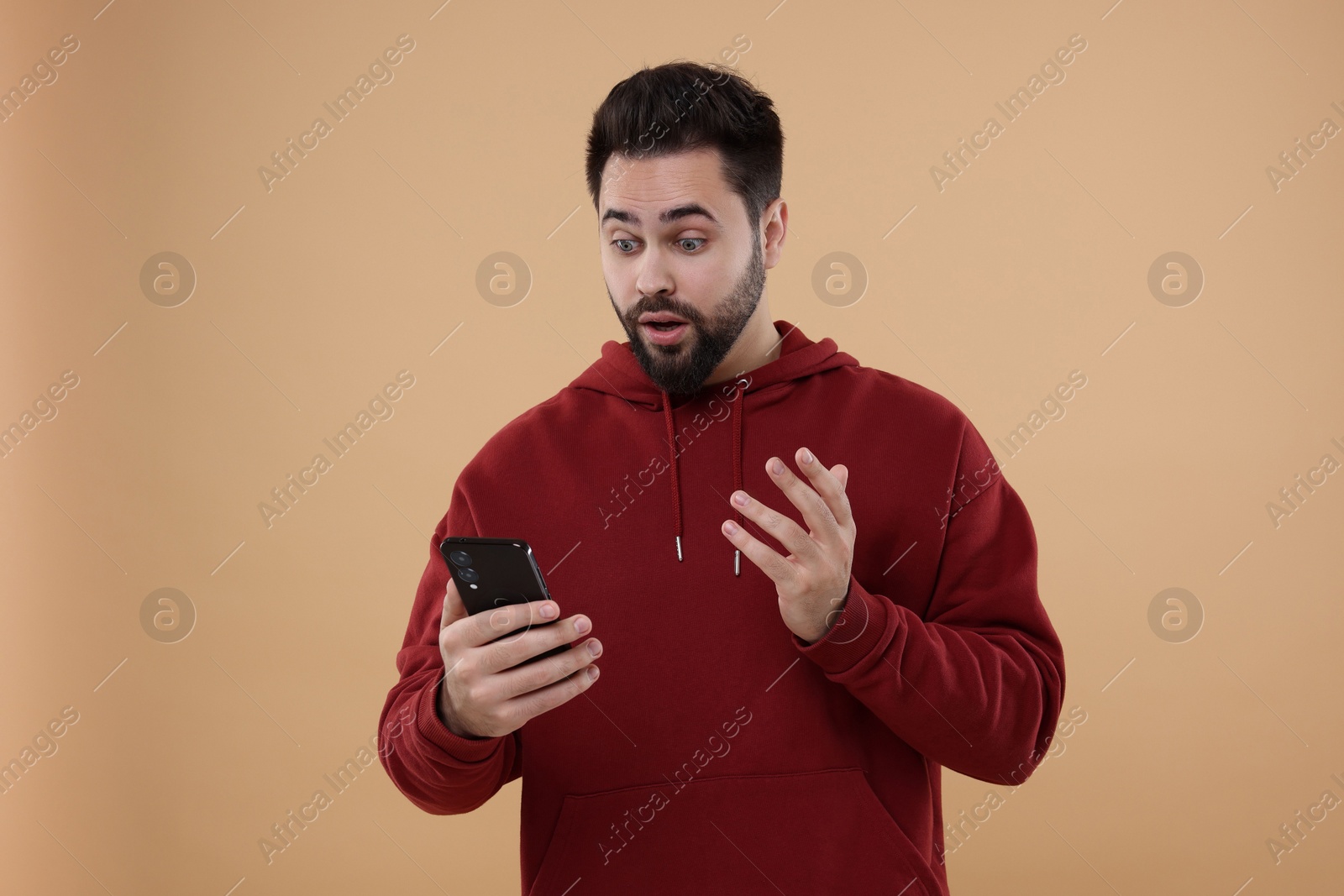 Photo of Shocked young man using smartphone on beige background