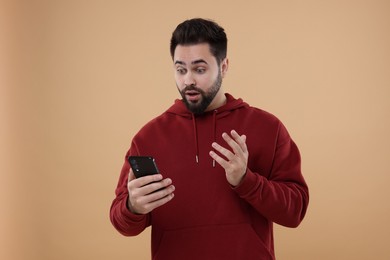 Photo of Shocked young man using smartphone on beige background