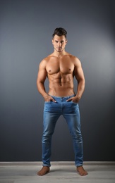 Photo of Shirtless young man in stylish jeans near grey wall