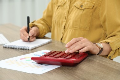 Photo of Professional accountant using calculator at wooden desk in office, closeup