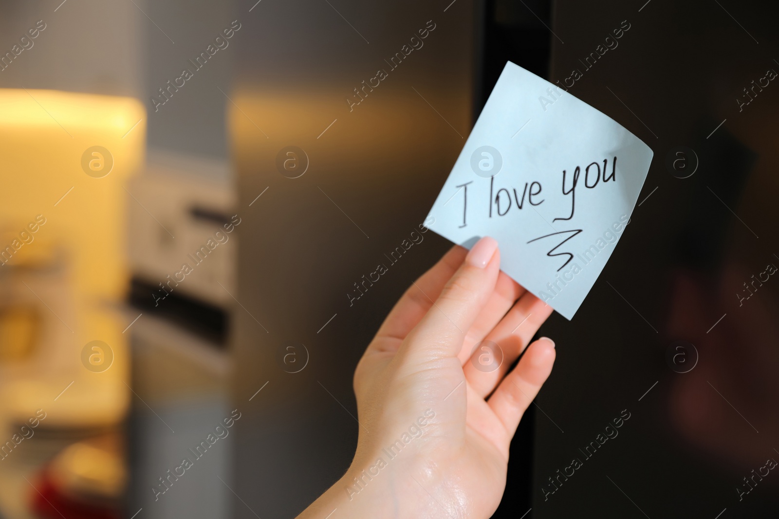 Photo of Woman with sticky note saying I Love You near fridge door, closeup. Romantic message