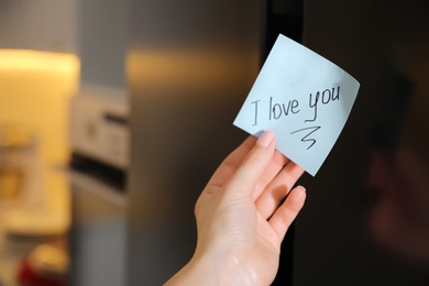 Photo of Woman with sticky note saying I Love You near fridge door, closeup. Romantic message