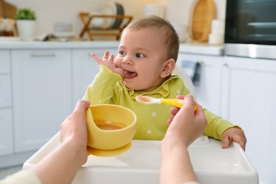 Photo of Mother feeding her cute little baby in kitchen