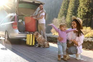 Photo of Mother with her daughter, man and dog near car outdoors. Family traveling with pet