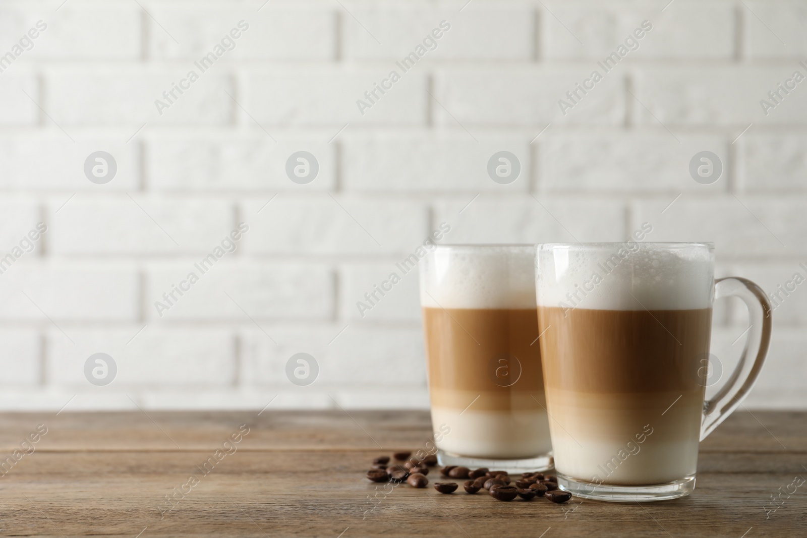 Photo of Hot coffee with milk in glass cups and beans on wooden table. Space for text