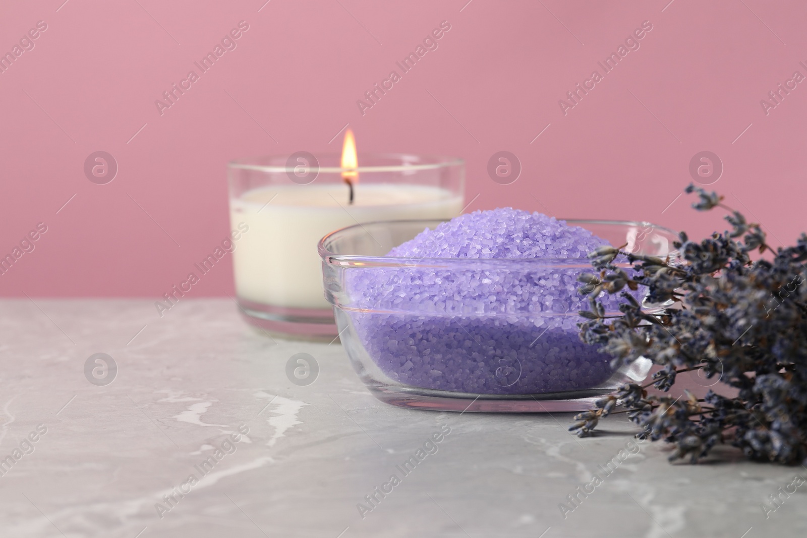 Photo of Violet sea salt in bowl, lavender flowers and burning candle on grey marble table. Space for text