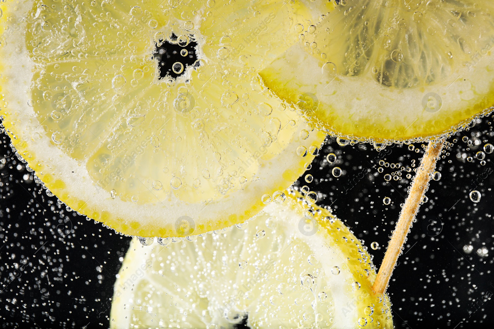 Photo of Juicy lemon slices in soda water against black background, closeup