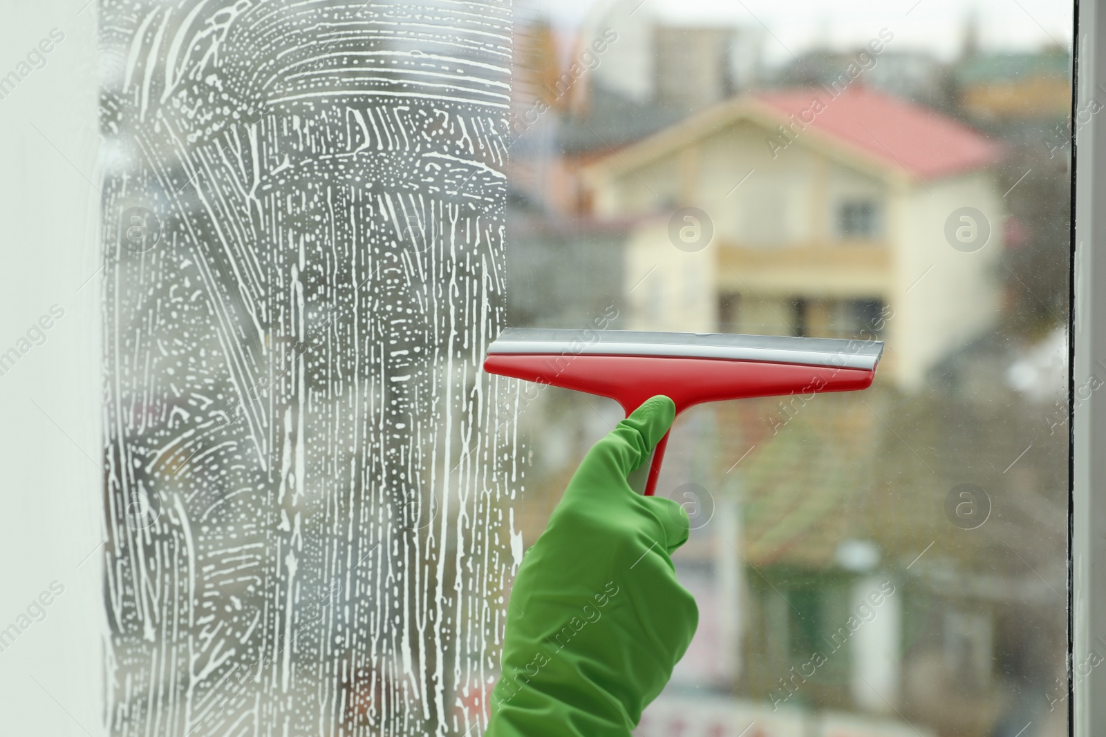 Photo of Woman cleaning window with squeegee indoors, closeup