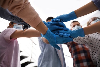 Photo of Group of people in blue medical gloves stacking hands indoors, closeup