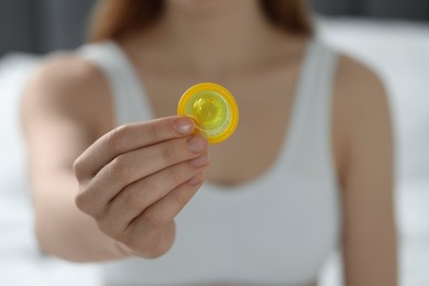Woman holding condom indoors, closeup. Safe sex