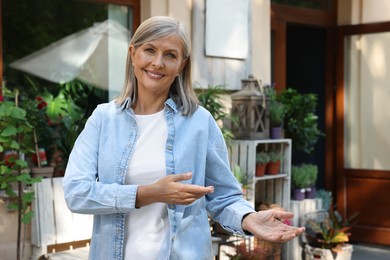 Happy business owner inviting to come into her flower shop outdoors, space for text