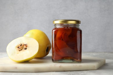 Photo of Tasty homemade quince jam in jar and fruits on grey textured table