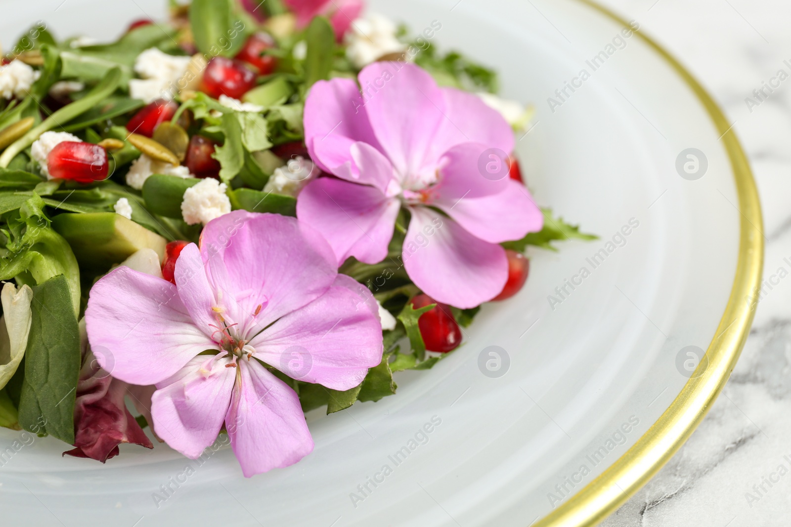 Photo of Fresh spring salad with flowers on white marble table, closeup