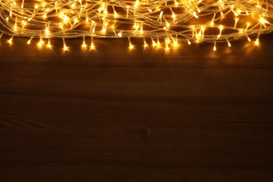 Photo of Beautiful glowing Christmas lights on wooden table, top view. Space for text