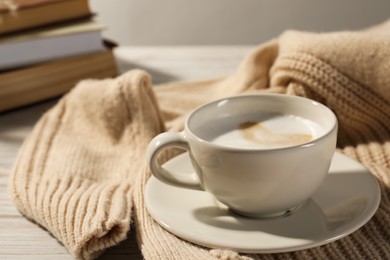 Cup of tasty coffee near sweater on white wooden table