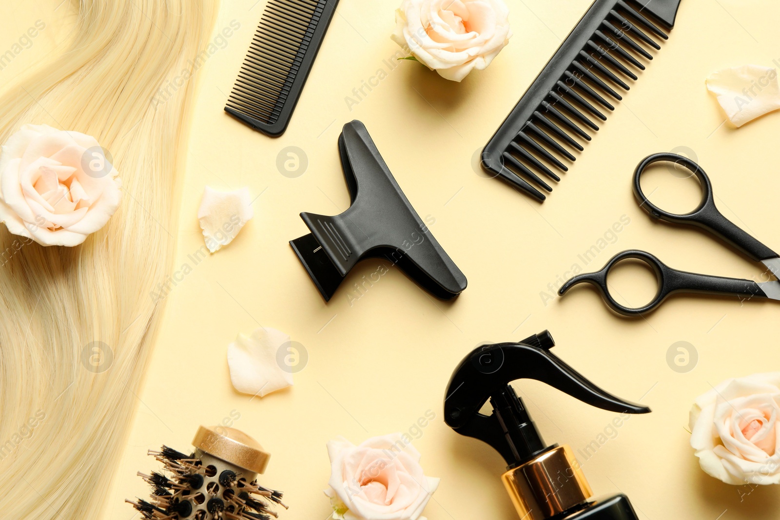 Photo of Flat lay composition with different hairdresser tools and flowers on pale yellow background