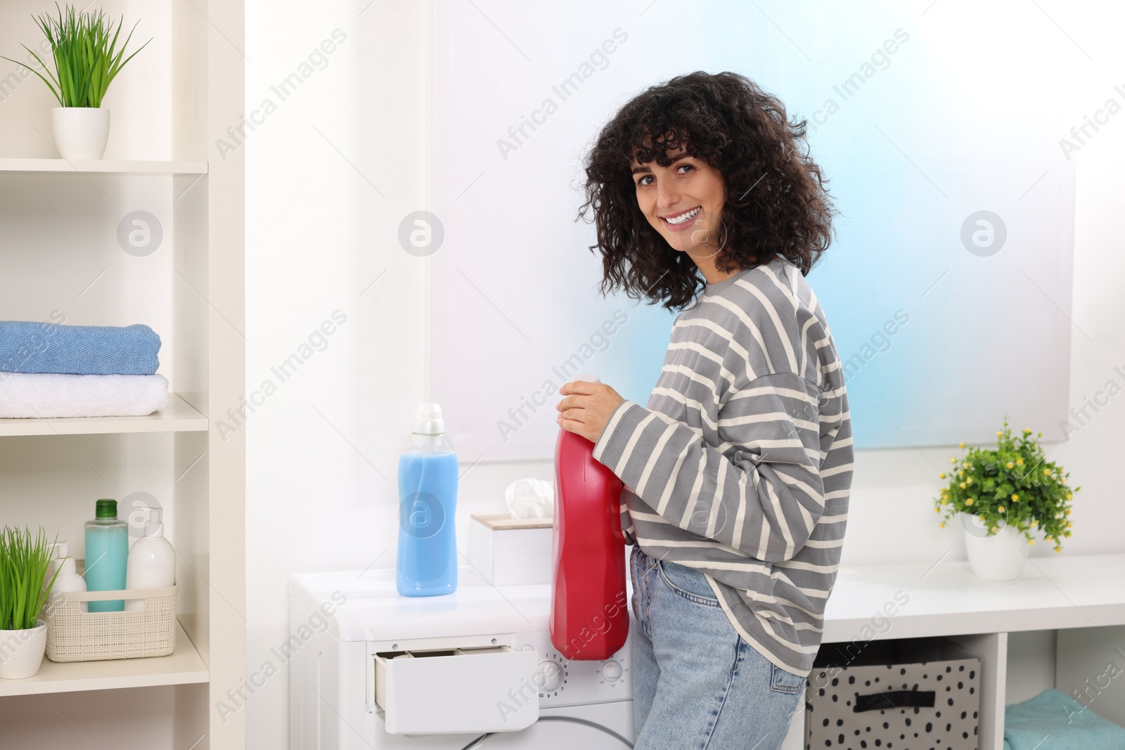 Photo of Happy woman with laundry detergent near washing machine indoors
