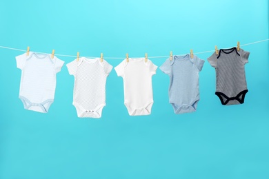 Photo of Colorful baby onesies hanging on clothes line against blue background. Laundry day