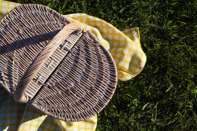 Photo of Picnic basket with checkered tablecloth on green grass, top view. Space for text