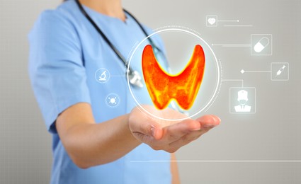 Image of Diagnosis and treatment of thyroid diseases. Endocrinologist holding virtual scheme with unhealthy gland and icons on light grey background, closeup