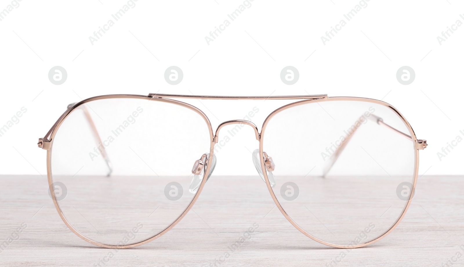 Photo of Stylish glasses with metal frame on wooden table against white background