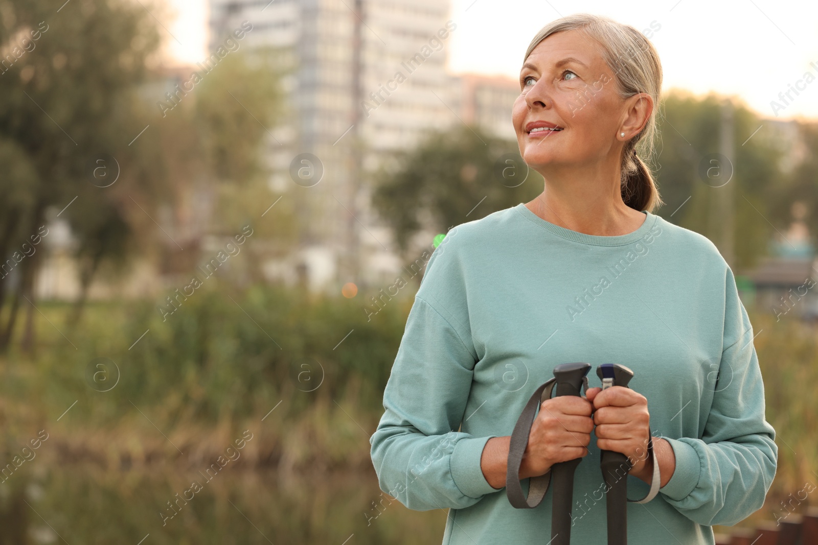 Photo of Senior woman with Nordic walking poles outdoors, space for text