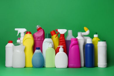 Many bottles of different detergents on green background. Cleaning supplies