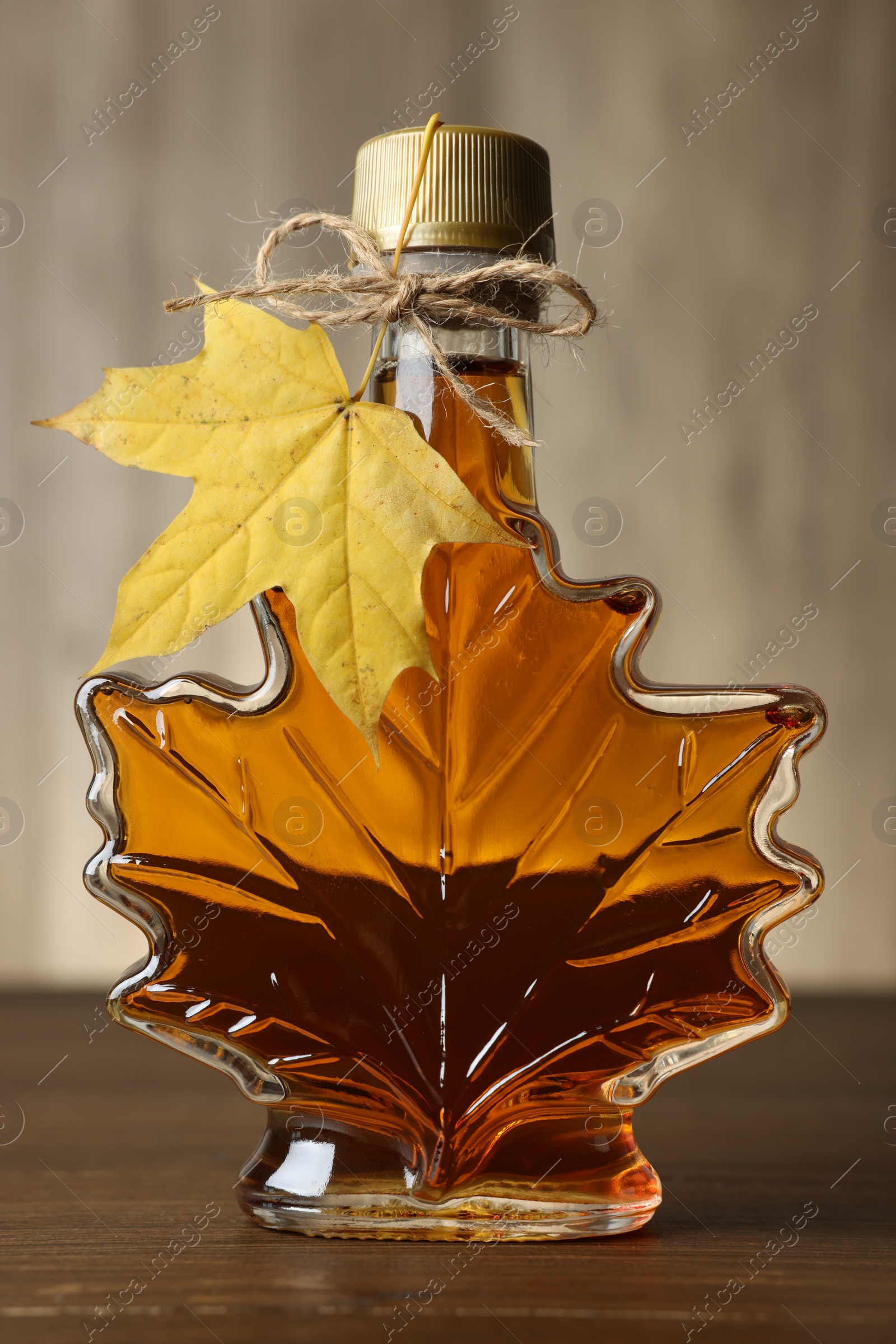 Photo of Leaf shaped bottle of tasty maple syrup on wooden table