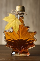 Leaf shaped bottle of tasty maple syrup on wooden table