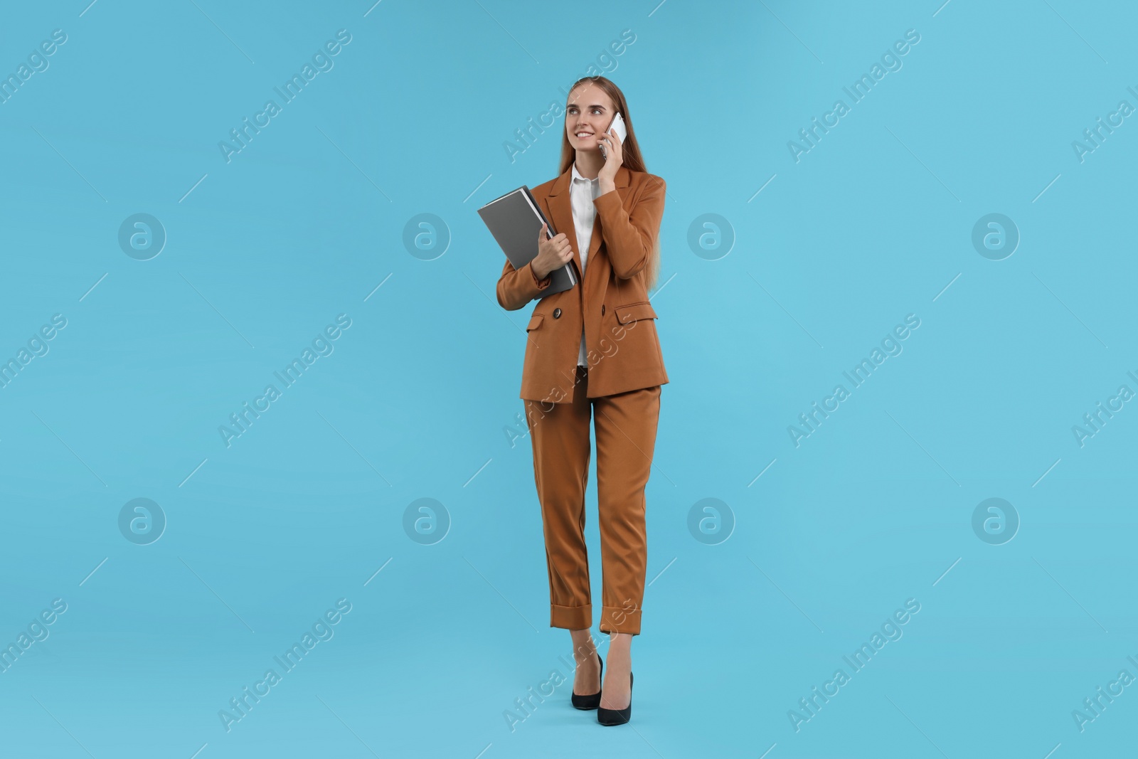 Photo of Happy young secretary with folders talking on smartphone against light blue background