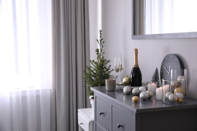 Photo of Christmas tree and decor on chest of drawers indoors. Interior design