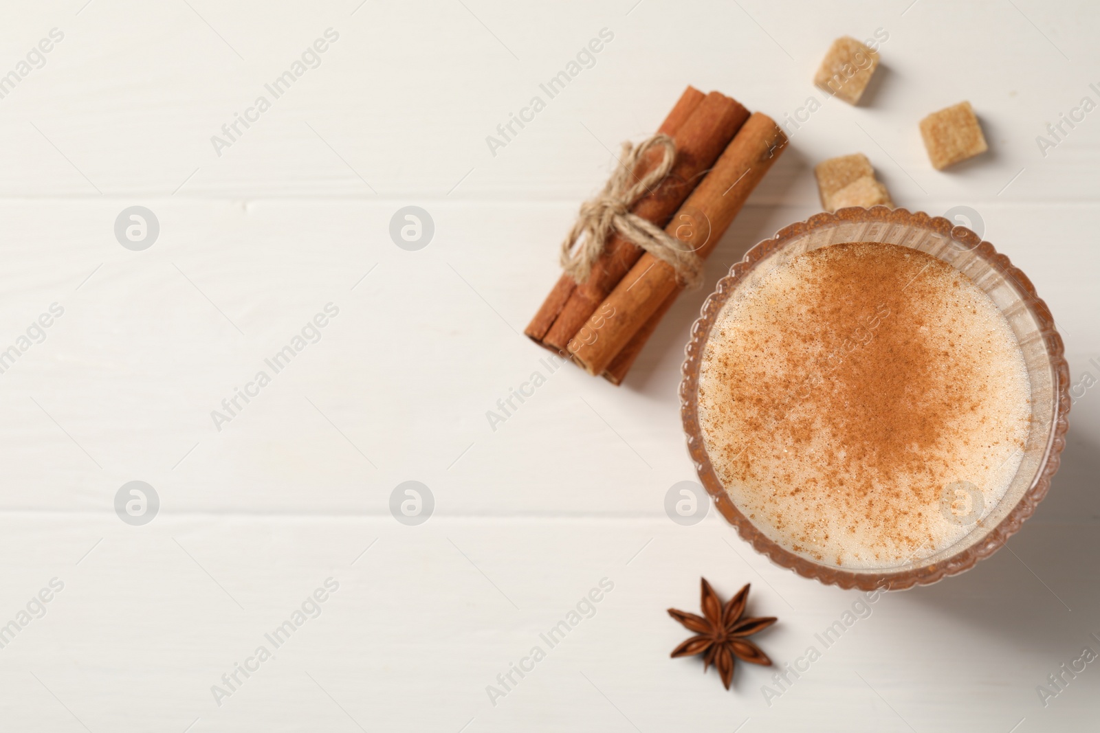 Photo of Delicious eggnog with anise and cinnamon on white wooden table, top view. Space for text
