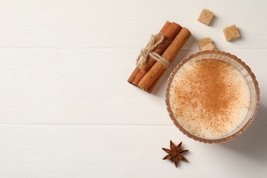 Delicious eggnog with anise and cinnamon on white wooden table, top view. Space for text