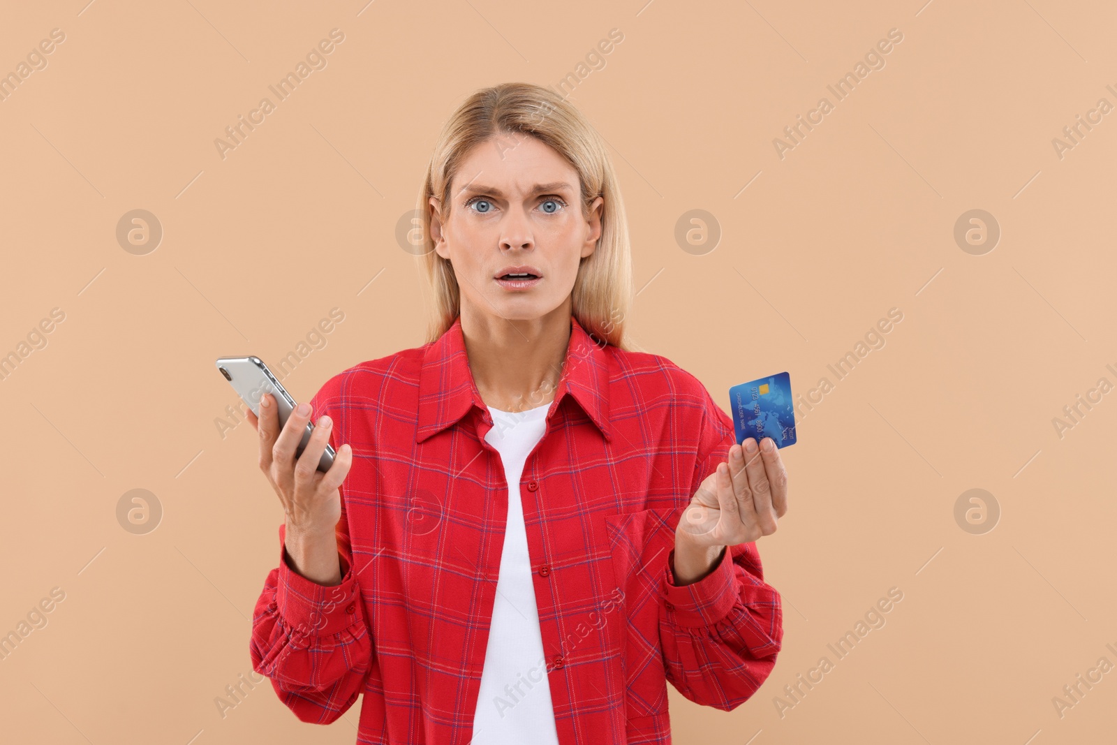 Photo of Stressed woman with credit card and smartphone on beige background. Be careful - fraud