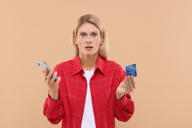 Stressed woman with credit card and smartphone on beige background. Be careful - fraud