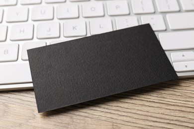 Photo of Blank black business card and computer keyboard on wooden table, closeup. Mockup for design