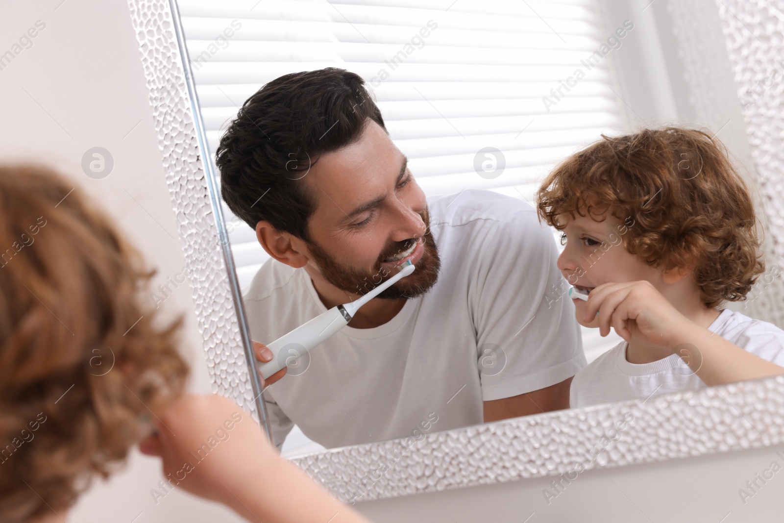 Photo of Father and his son brushing teeth together near mirror in bathroom