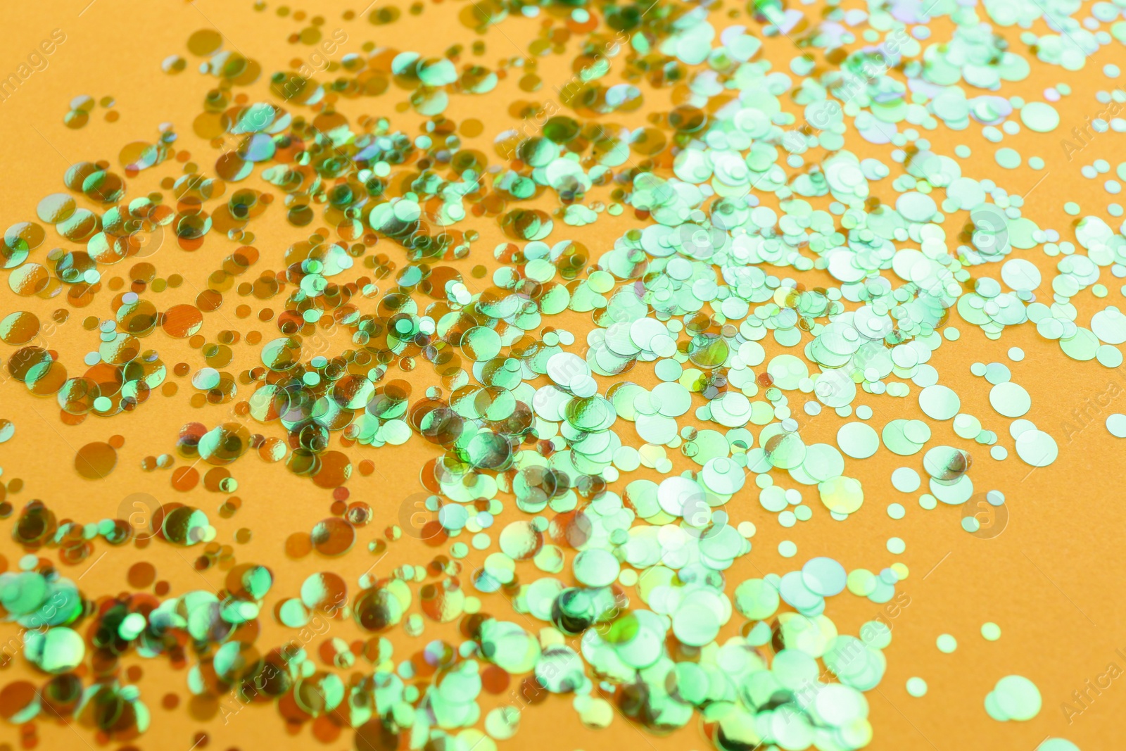 Photo of Shiny bright glitter scattered on orange background