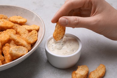 Woman dipping crispy rusk in sauce at light table, closeup