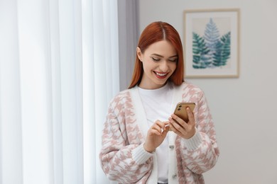Photo of Happy woman sending message via smartphone at home. Space for text