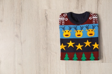 Photo of Warm folded Christmas sweater on light wooden table, top view. Space for text