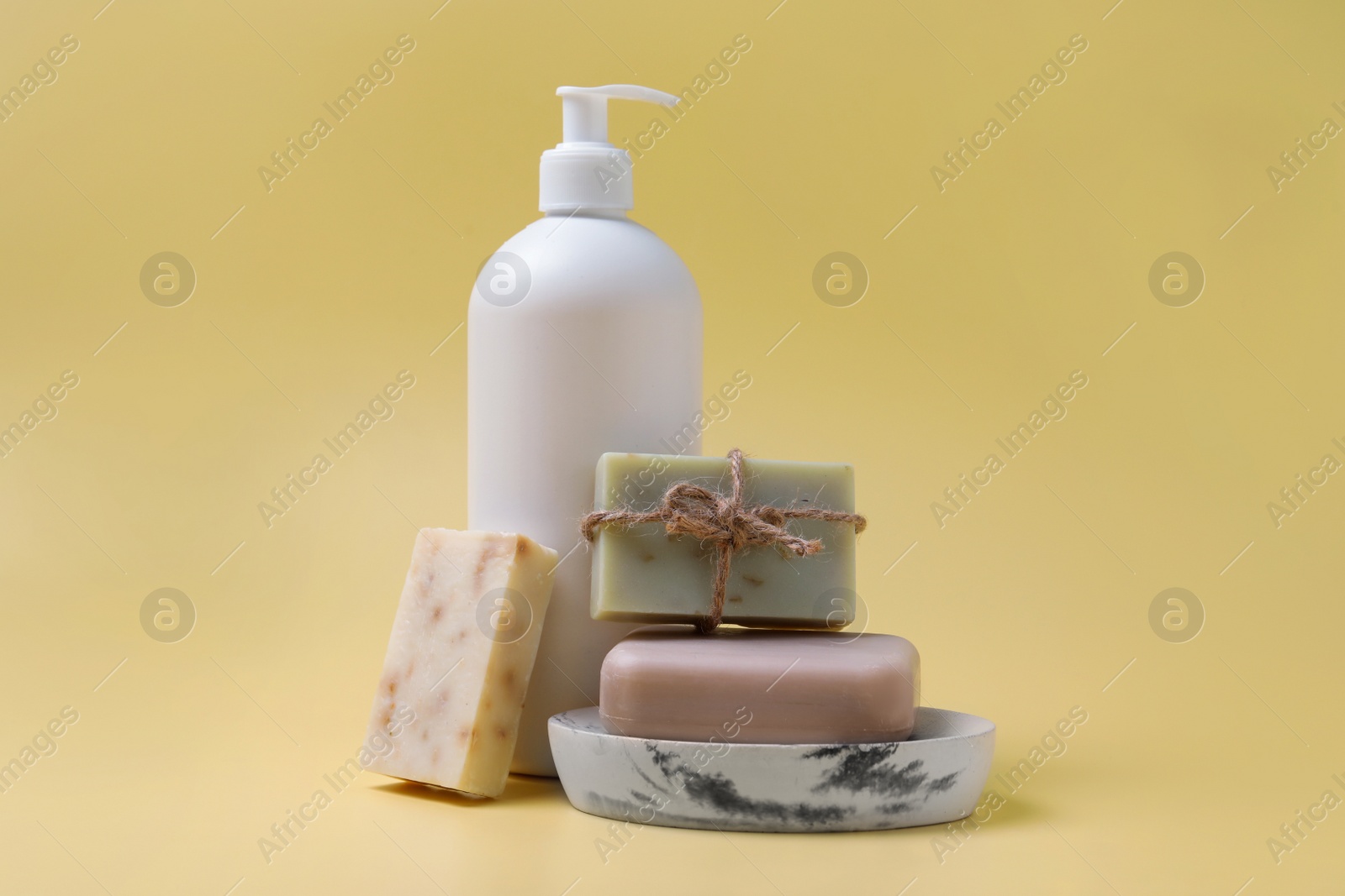 Photo of Soap bars and bottle dispenser on yellow background