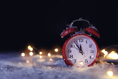 Photo of Alarm clock and Christmas lights on white snow outdoors, space for text. Midnight countdown