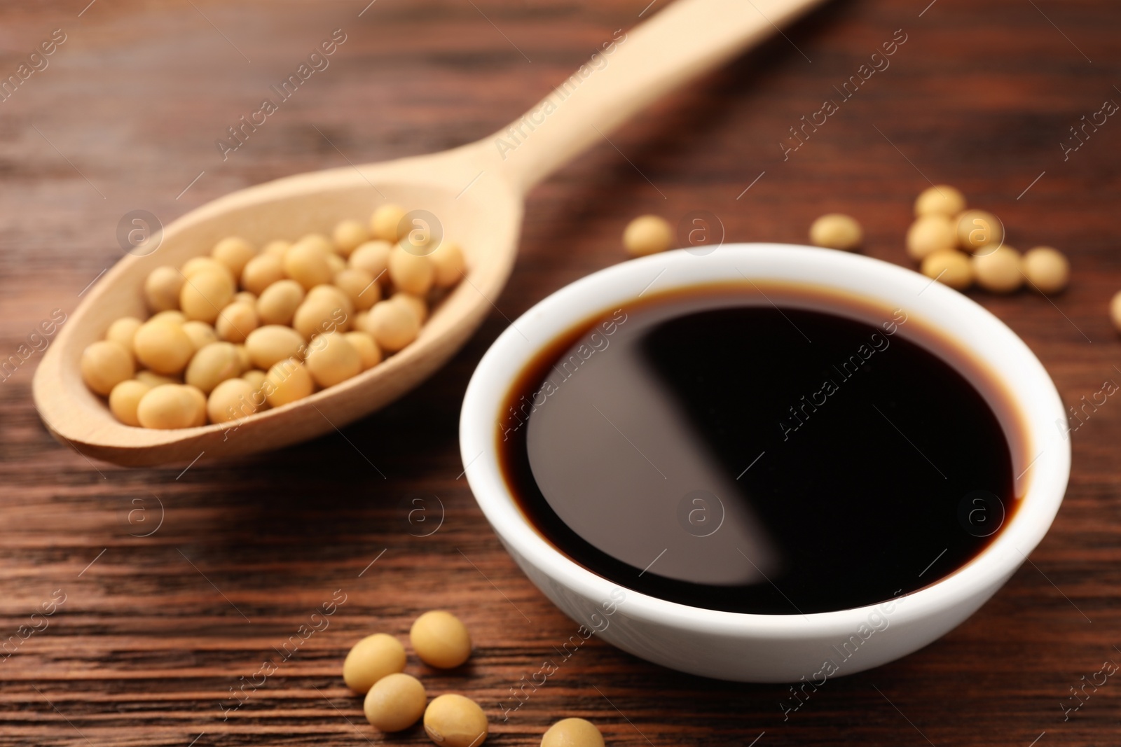 Photo of Soy sauce in bowl and soybeans on wooden table, closeup