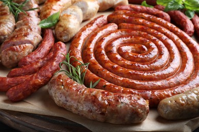 Photo of Different delicious sausages with herbs on wooden board, closeup. Assortment of beer snacks