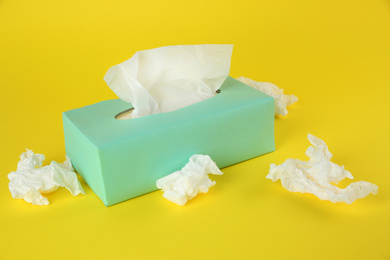 Photo of Used paper tissues and box on yellow background