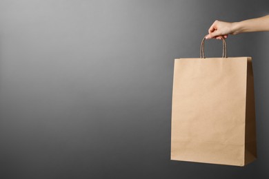 Photo of Woman holding kraft paper bag on grey background, closeup with space for text. Mockup for design