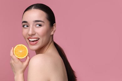 Photo of Beautiful young woman with piece of orange on pink background. Space for text