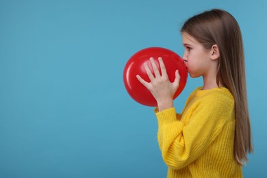 Photo of Cute girl inflating red balloon on light blue background, space for text