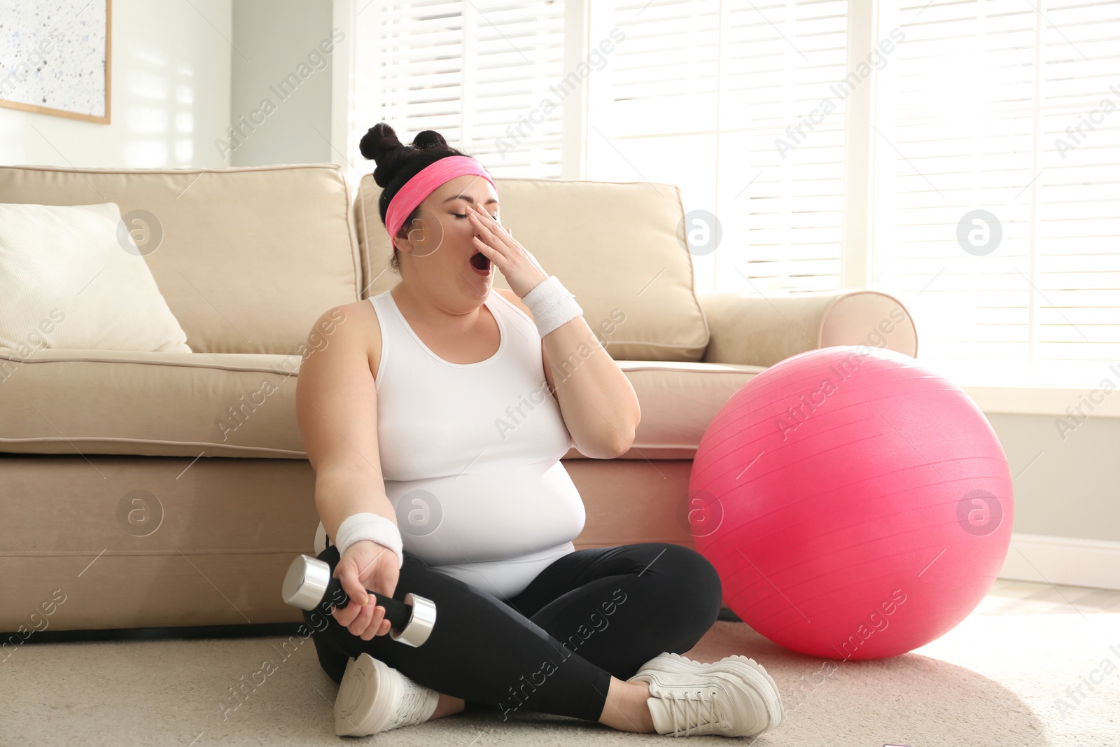 Photo of Lazy overweight woman with sport equipment on floor at home